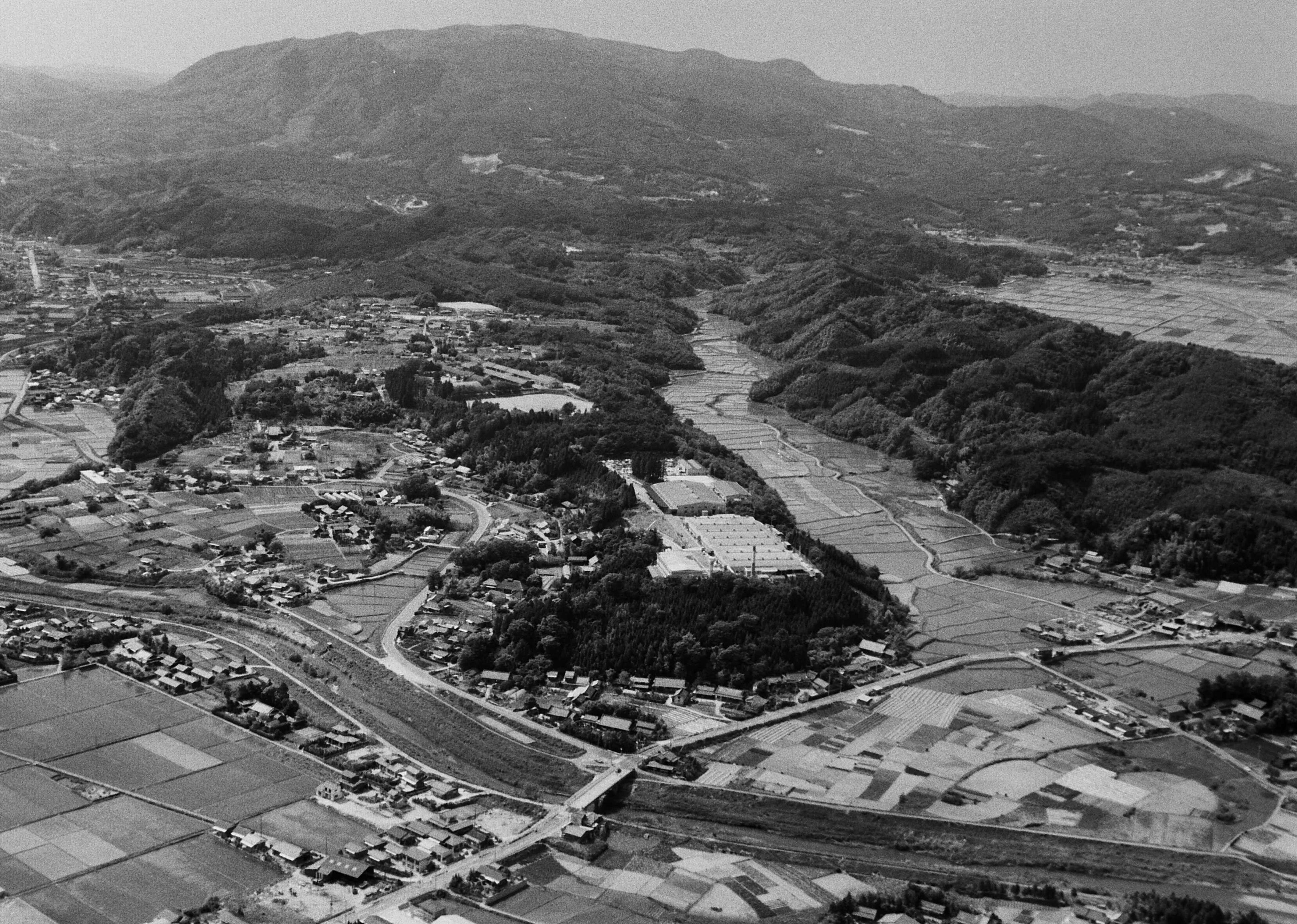 ■写真1-2　好間町小谷作（建設計画の東側）から見る団地予定地  丘陵地上に見えるのは、既設の工場。〔昭和50年代半ば　いわき市撮影〕